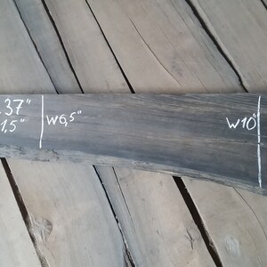 Op de afbeelding: Een donkergrijze houten plaat met witte markeringen die de afmetingen aangeven: L 37", T 1,5", B 9,5" en B 10".
