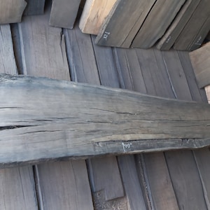 May include: A large, dark grey wooden plank with a rough, natural texture. The plank has several cracks and knots. The plank is marked with the measurements "L 75" and "119" in white.