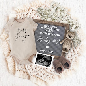 May include: A beige baby onesie with the name "Baby Jameson" and a heart graphic. A grey letter board announces "We're due with Baby #2 April 2026". The image includes a sonogram, a teddy bear, and baby booties.