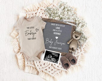 Könnte beinhalten: Ein graues Buchstabenbrett mit dem Text "Made with lots of love and a little science Baby Jameson Due August 2025". Ein gehäkelter Teddybär, ein Paar braune Babyschuhe und ein Ultraschallbild sind um das Buchstabenbrett herum angeordnet. Ein beiger Strampler mit dem Text "The little Embryo that could" liegt auf einer beigen Decke.