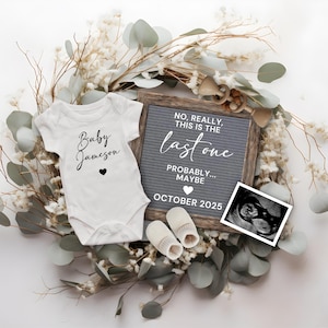 Peut inclure: Un body blanc pour bébé avec l'inscription "Baby Jameson", un tableau de lettres gris avec du texte, une échographie et des chaussons pour bébé, le tout agrémenté de décorations florales. Le tableau de lettres indique "NO, REALLY, THIS IS THE last one PROBABLY... MAYBE OCTOBER 2025."