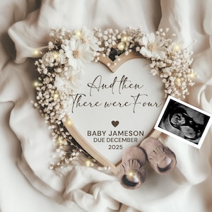 May include: A heart-shaped wooden frame with the text "And then There were Four" and "Baby Jameson Due December 2025". The frame is decorated with white flowers and fairy lights. A sonogram image and baby shoes are also included.