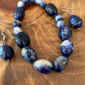 May include: A set of blue and white gemstone earrings and a bracelet. The earrings are teardrop shaped and the bracelet is made of oval-shaped beads.