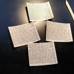 May include: Four pieces of paper with Hebrew text written on them, and two white feathers on a black surface.