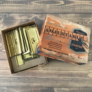May include: A set of brass stencils inside a cardboard box labeled Reese's Adjustable Lockedge Brass Stencils. The box features tan, blue, and black text with an illustration of a hand holding a stencil. The brass pieces are rectangular with interlocking edges.