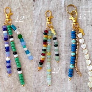 May include: Three beaded keychains with gold-colored clasps. One features purple, blue, green, and white beads. Another has red, green, yellow, and black beads. The third has blue, turquoise, gold, and heart-shaped beads.