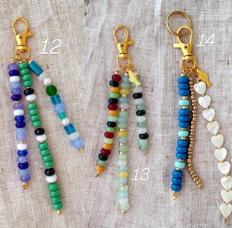 May include: Three beaded keychains with gold-colored clasps. One features purple, blue, green, and white beads. Another has red, green, yellow, and black beads. The third has blue, turquoise, gold, and heart-shaped beads.