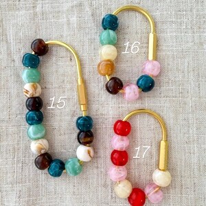 May include: Three keychains with gold-colored metal hardware and colorful beaded accents. The keychains are labeled with the numbers 15, 16, and 17. The beads are in shades of teal, brown, pink, red, and white.