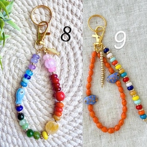 May include: Two beaded keychains with gold-colored hardware. One features a rainbow of beads with a blue fish charm. The other has orange beads with blue fish charms and a rainbow beaded accent. Both have a gold fish charm.