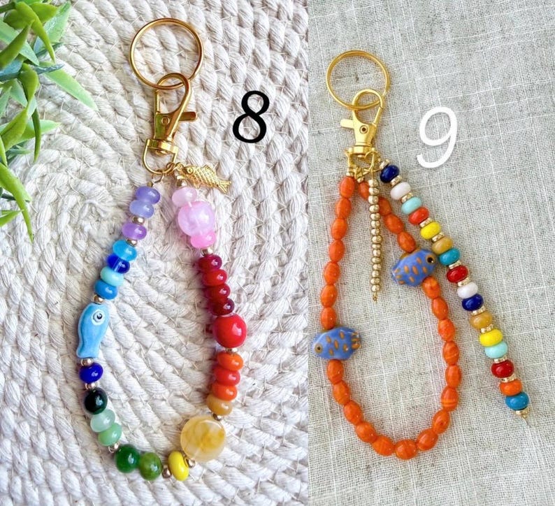 May include: Two beaded keychains with gold-colored hardware. One features a rainbow of beads with a blue fish charm. The other has orange beads with blue fish charms and a rainbow beaded accent. Both have a gold fish charm.