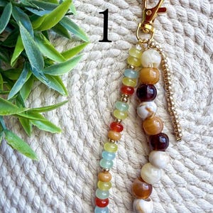 May include: A beaded keychain with a gold-colored clasp and hardware. The keychain features a variety of colorful beads, including yellow, blue, orange, and brown. The beads are strung together in a decorative pattern, creating a stylish accessory.