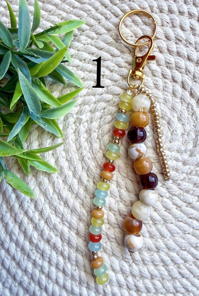 May include: A beaded keychain with a gold-colored clasp and hardware. The keychain features a variety of colorful beads, including yellow, blue, orange, and brown. The beads are strung together in a decorative pattern, creating a stylish accessory.