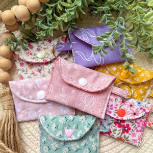 May include: Assortment of small fabric pouches with floral patterns and key rings. The pouches are quilted and have a button closure. The colors include pink, green, purple, yellow, and white.