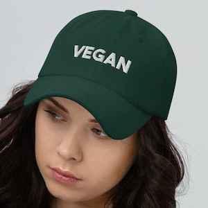 May include: A dark green baseball cap with the word "VEGAN" embroidered in white on the front.