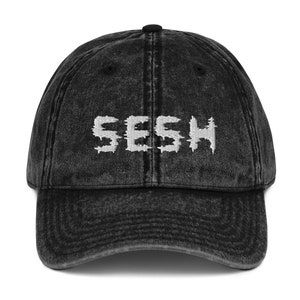 May include: A black vintage washed denim baseball cap with white embroidered text that reads "SESH".