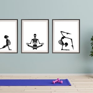 May include: Three framed art prints featuring black and white skeleton illustrations in yoga poses. A blue yoga mat and pink dumbbells are on the floor. A potted plant is to the right.
