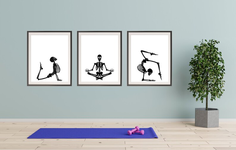 May include: Three framed art prints featuring black and white skeleton illustrations in yoga poses. A blue yoga mat and pink dumbbells are on the floor. A potted plant is to the right.