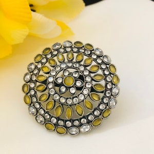 Peut inclure: Une bague en argent avec un motif rond présentant une fleur jaune centrale entourée de petites pierres blanches et de plus grandes pierres jaunes.