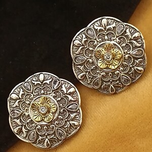 May include: A pair of silver and gold earrings with a floral design and clear stones. The earrings are round and have a delicate, intricate pattern.