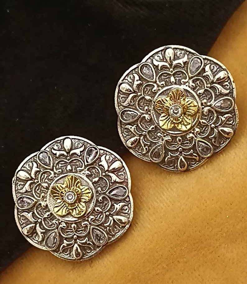 May include: A pair of silver and gold earrings with a floral design and clear stones. The earrings are round and have a delicate, intricate pattern.