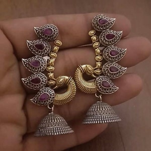 Pode incluir: Um par de brincos de prata e ouro com um pingente de sino. Os brincos apresentam um design de m&uacute;ltiplos pingentes em forma de l&aacute;grima com pedras vermelhas e um design de pav&atilde;o.