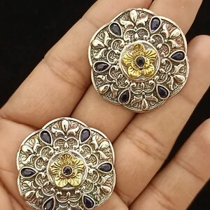 May include: A pair of silver and gold earrings with a floral design and blue gemstones.