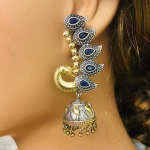 Pode incluir: Brincos em tom prateado e dourado com um design de pav&atilde;o e pedras azuis. Os brincos t&ecirc;m um charme de sino pendurado.