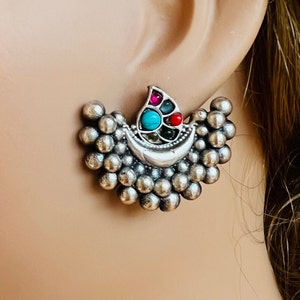 May include: Silver earrings with a crescent moon design and a cluster of colourful gemstones in the centre. The earrings are made of small silver beads.