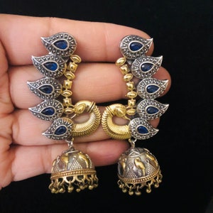 Pode incluir: Um par de brincos de prata e ouro com pedras azuis e um pingente de sino.