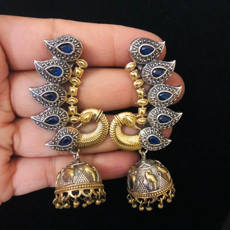 Pode incluir: Um par de brincos de prata e ouro com pedras azuis e um pingente de sino.