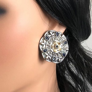 May include: Silver and gold tone earrings with a circular design featuring a floral motif and blue gemstones.