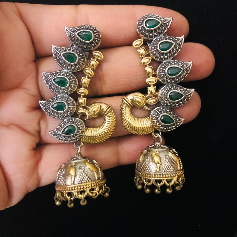 Pode incluir: Um par de brincos de prata e ouro com pedras verdes. Os brincos t&ecirc;m a forma de uma pena de pav&atilde;o e t&ecirc;m um pingente em forma de sino.