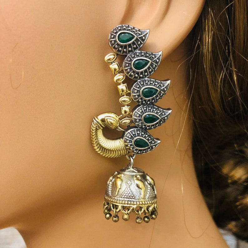 Pode incluir: Brincos em tom dourado e prateado com pedras verdes e design de pav&atilde;o. Os brincos t&ecirc;m um charme de sino pendurado.