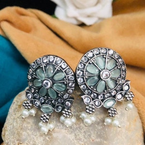 May include: A pair of silver earrings with a floral design. The earrings have a round centre with a white stone surrounded by smaller white stones. The centre is surrounded by a ring of larger, light blue stones. The earrings have a dangling design with three white pearls on each side.