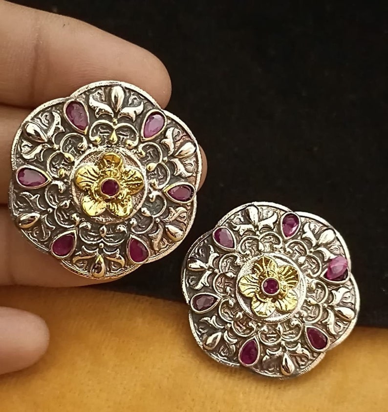 May include: A pair of silver and gold earrings with intricate floral designs and pink gemstones.