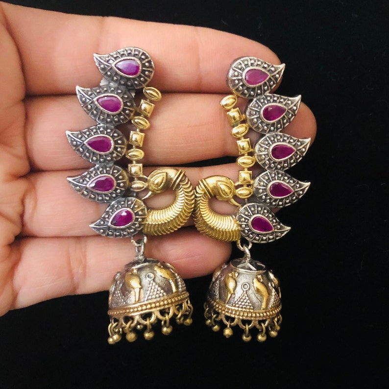 Pode incluir: Um par de brincos de prata e ouro com pedras rosa e um pingente de sino.