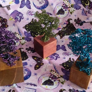 May include: Five wire-wrapped trees with different colored beads and crystals, displayed on wooden bases. The trees are arranged on a pink and purple patterned fabric.