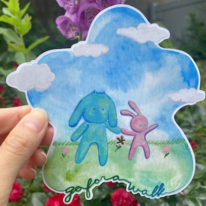 May include: A watercolor sticker featuring two cartoon characters, a blue dog and a pink rabbit, walking together in a green field with a blue sky and white clouds. The text "go for a walk" is written in green at the bottom of the sticker.