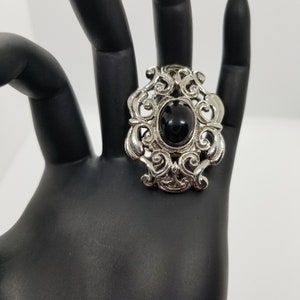 May include: A silver ring with a black stone set in a filigree design.