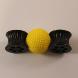 Peut inclure: Trois jauges d'oreille en plastique noir avec une surface textur&eacute;e et un motif circulaire. Les jauges d'oreille sont dispos&eacute;es en rang&eacute;e avec une boule jaune au centre.