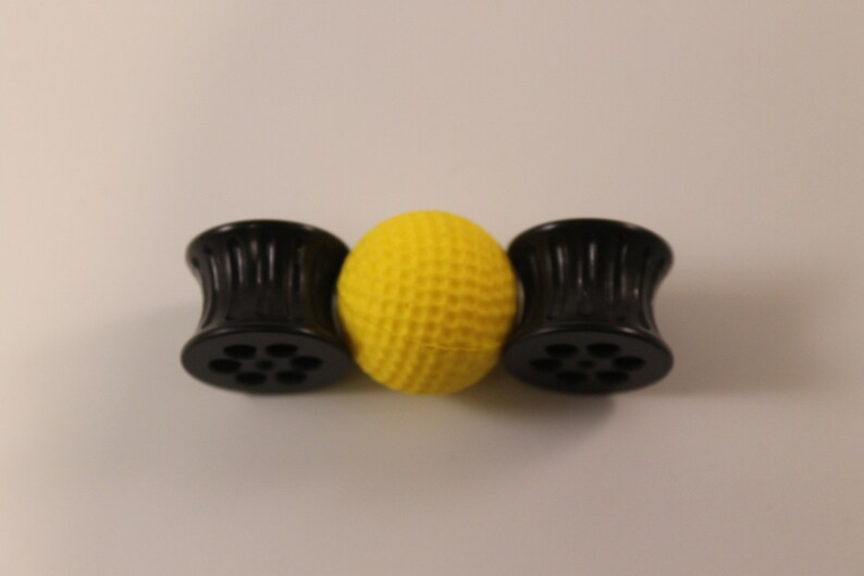 Peut inclure: Trois jauges d'oreille en plastique noir avec une surface textur&eacute;e et un motif circulaire. Les jauges d'oreille sont dispos&eacute;es en rang&eacute;e avec une boule jaune au centre.