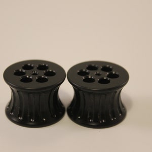 Peut inclure: Une paire de jauges d'oreille noires avec un design cannel&eacute; et un dessus circulaire avec six trous.