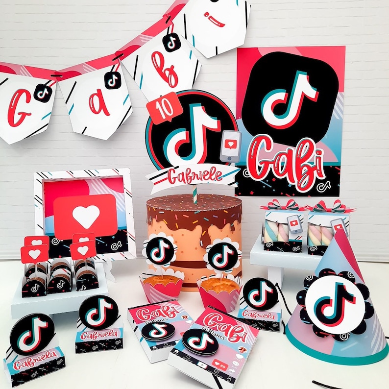 May include: A collection of party decorations featuring a TikTok theme. Includes a cake, cupcakes, gift boxes, and a banner with the TikTok logo and the name "Gabi". The color scheme is red, black, white, and blue.