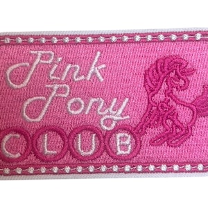 May include: A pink embroidered patch with the words "Pink Pony Club" in white script and block letters. A pink pony silhouette is on the right. The patch has a white dotted border.