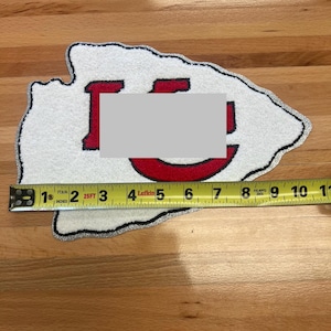 May include: A white and red patch in the shape of an arrowhead, with a silver border. The patch measures approximately 8 inches long. The patch has a red "I" and "U" design.