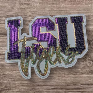 May include: LSU Tigers logo patch with purple and gold sequins. The patch is made of felt and has a white background.