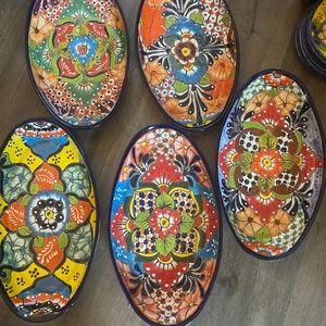 Op de afbeelding: Vijf ovale keramische serveerschalen met kleurrijke bloemmotieven. De schalen zijn versierd met felle kleuren, waaronder rood, oranje, geel, groen, blauw en zwart. De schalen zijn allemaal iets anders, maar ze hebben allemaal een vergelijkbare stijl.