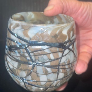 May include: A clear glass cup with a brown and white marbled design and black lines throughout.