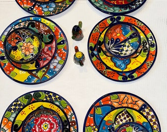 May include: Set of six colourful ceramic dinner plates with matching bowls. Each plate features a different floral design with blue, yellow, red, and green accents. The bowls are smaller and have a similar floral design.