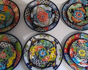 May include: Set of six colourful ceramic plates with floral designs. Each plate features a different pattern with vibrant colours like blue, green, yellow, red, and white. The plates are perfect for adding a touch of Mexican style to your dining table.